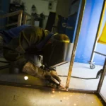 Soudeur en train de souder une pièce métallique, avec une gerbe d'étincelles